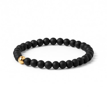An angled studio shot of the 6mm matte black onyx bead bracelet with a 14k gold-filled accent, emphasizing the architectural quality and seamless elastic cord construction.
