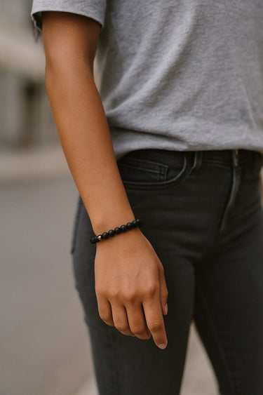 A close-up lifestyle view of the 6mm matte black onyx bracelet on a model's wrist, highlighting the sophisticated contrast between the matte stones and the polished gold accent bead.
