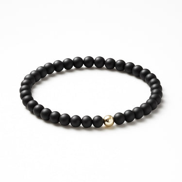 An angled studio shot of the 6mm matte black onyx bead bracelet with a sterling silver accent, emphasizing the architectural quality and seamless elastic cord construction.
