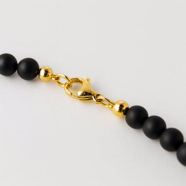 A macro close-up of the professional-grade 14K gold-filled lobster clasp closure on the 6mm Matte Black Onyx necklace.
