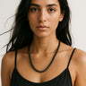 A lifestyle shot of a female model wearing a 6mm Matte Black Onyx round bead necklace against a black top, highlighting its muted texture and elegant drape.
