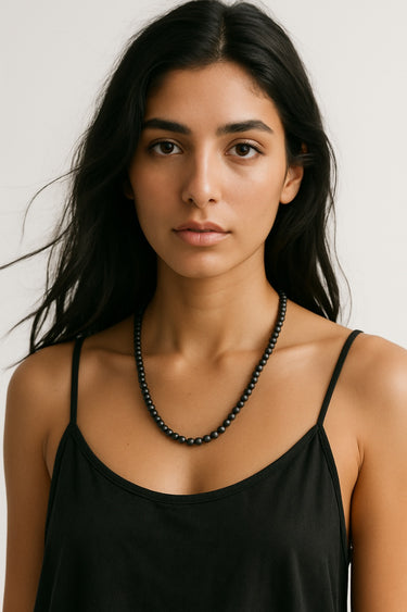 A lifestyle shot of a female model wearing a 6mm Matte Black Onyx round bead necklace against a black top, highlighting its muted texture and elegant drape.
