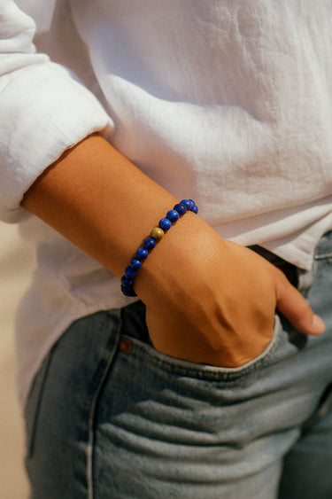 A lifestyle shot of a model wearing a 6mm natural blue lapis lazuli bead bracelet, showcasing the deep ultramarine tones and its effortless, stackable silhouette for everyday luxury.
