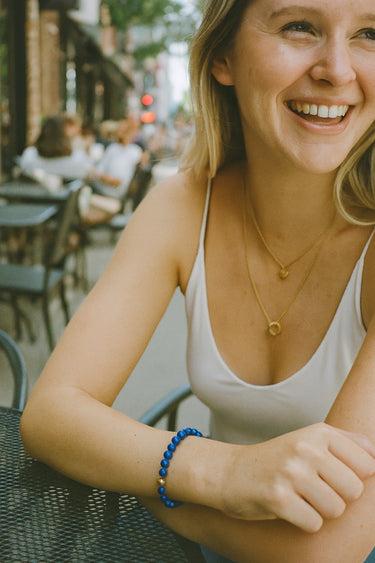 A lifestyle view of the 6mm blue lapis lazuli bead bracelet on a model at a café, emphasizing its versatile appeal and comfortable drape for a refined, daily look.
