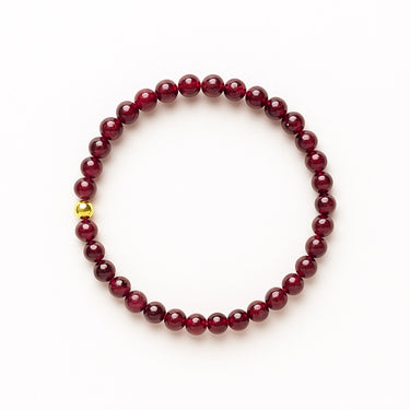 A studio hero shot of a 6mm natural garnet bead bracelet featuring a 14K gold-filled accent bead, highlighting the deep wine-red gemstone tones and high-luster finish.
