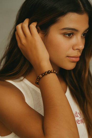 A lifestyle portrait of a model wearing a 6mm Tiger's Eye bead bracelet, showcasing the warm earth tones and structural silhouette of the semi-precious stones.
