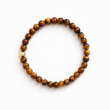 A studio hero shot of a women's 6mm Tiger's Eye bead bracelet featuring a single 14K gold-filled accent bead, arranged in a clean circle to highlight the chatoyant golden-brown bands of the natural stones.
