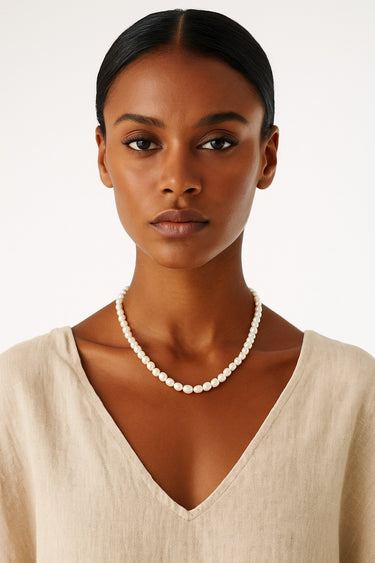 A woman wearing the 7-8mm pearl necklace against a beige v-neck top, highlighting the natural, iridescent glow of the pearls and their refined architectural presence.
