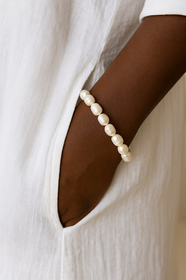A lifestyle shot of a model wearing a 7-8mm white baroque freshwater pearl bracelet, showcasing the unique organic shapes and elegant luster against a white linen outfit.
