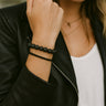 A lifestyle shot of a model wearing the 8mm black lava bead bracelet stacked with a minimalist black cuff, showcasing its architectural silhouette and modern luxury aesthetic paired with a leather jacket.
