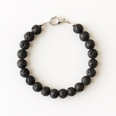 A studio hero shot of a women's 8mm black lava round bead bracelet featuring a structural sterling silver lobster clasp, highlighting the organic, porous texture of the volcanic stones.
