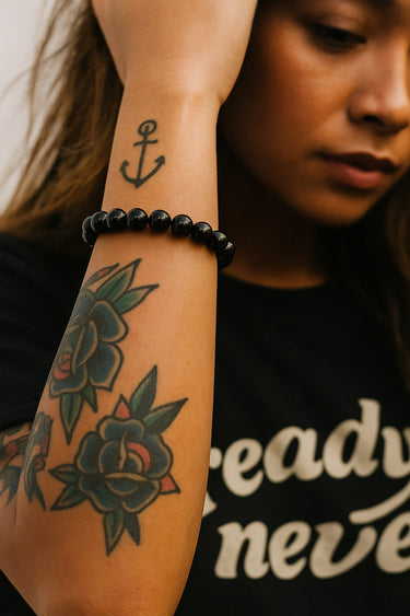 A lifestyle shot of a model wearing a women's 8mm gloss black onyx bead bracelet, showcasing the high-shine reflective finish of the stones against a graphic black tee.
