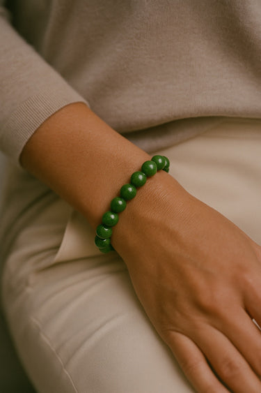 A lifestyle shot of a model wearing a women's 8mm green jade bead bracelet, showcasing the vibrant natural stones and structural silhouette against neutral tones.
