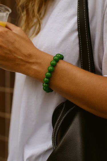 A lifestyle image of a model wearing the 8mm green jade bead bracelet, demonstrating its sophisticated presence and natural color depth in outdoor lighting.
