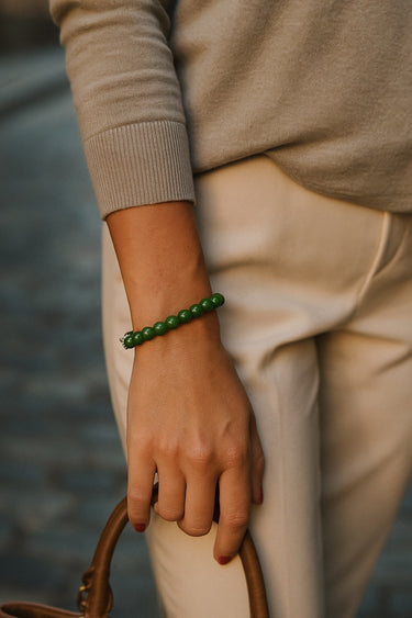 A candid lifestyle shot of a model's wrist featuring the 8mm green jade bracelet, emphasizing its modern luxury aesthetic and effortless drape.
