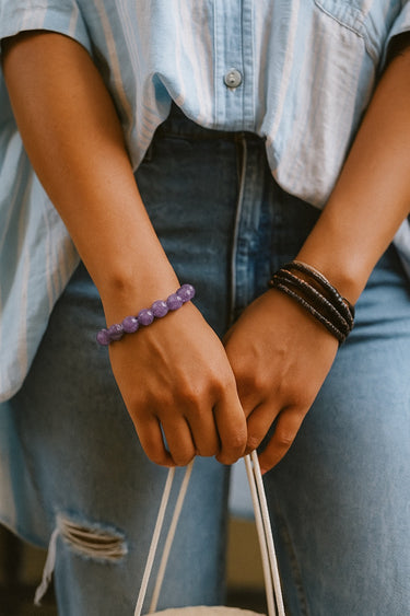 A lifestyle shot of a model wearing an 8mm amethyst bead bracelet paired with a dark bead stack, showcasing its rich color and versatile, layered luxury aesthetic.
