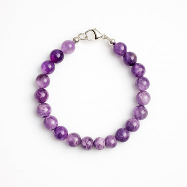 A studio hero shot of a women's 8mm natural amethyst bead bracelet with a sterling silver lobster clasp, highlighting the vibrant purple gemstone tones and high-polish finish.
