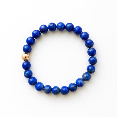 A studio hero shot of a women's 8mm natural blue lapis lazuli bead bracelet featuring a single 14K gold-filled accent bead, showcasing the deep royal blue stones and high-luster finish.
