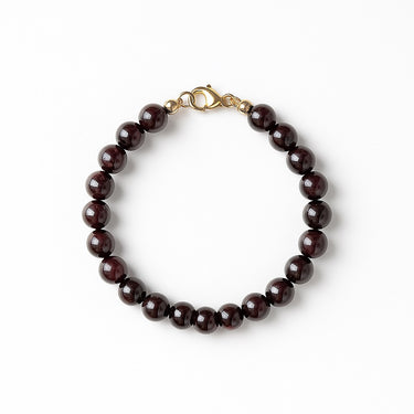 A studio hero shot of a women's 8mm natural garnet bead bracelet with a 14K gold-filled lobster clasp, highlighting the deep wine-red gemstone tones and high-polish finish.
