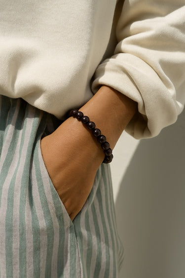 A lifestyle shot of a model wearing the 8mm garnet bead bracelet, showcasing its sophisticated rich color and effortless, stackable design for everyday luxury.
