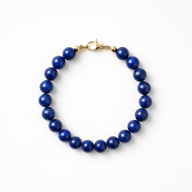 A studio hero shot of a women's 8mm natural lapis lazuli bead bracelet with a 14K gold-filled lobster clasp, highlighting the deep royal blue gemstone tones and high-polish finish.
