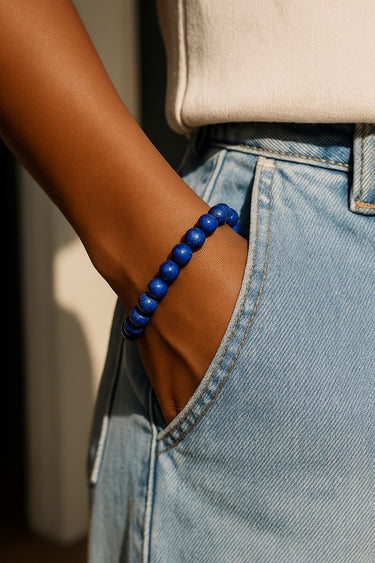 A lifestyle shot of a model wearing an 8mm lapis lazuli bead bracelet with her hand in a denim pocket, showcasing the vibrant blue color against casual wear.
