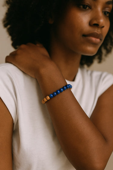 A lifestyle shot of a model wearing the blue lapis and sandalwood bracelet, demonstrating its natural, earthy aesthetic and comfortable elastic fit.
