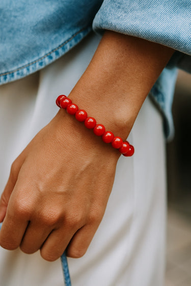 A lifestyle shot of a model wearing the 8mm red agate bead bracelet, showcasing its bold color and effortless, stackable silhouette for everyday luxury.

