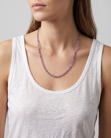 A model wearing a 4mm amethyst round bead necklace, showcasing the vibrant purple stones against a white tank top for an editorial, sophisticated look.