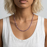Woman wearing a white tank top and a purple amethyst heishi beaded necklace with a plain background