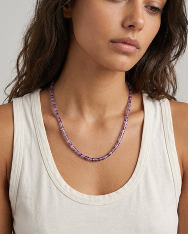 Woman wearing an amethyst beaded necklace against a neutral background