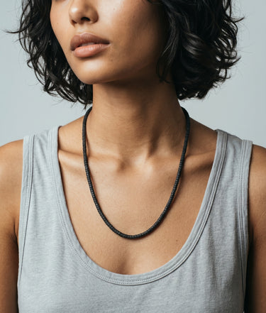 Model with a gray tank top wearing a black lava heishi necklace on a gray background