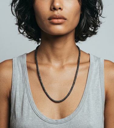 woman with a gray tank top wearing a black lava heishi necklace on a gray background