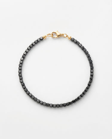 A studio product shot of a women's AAA natural black tourmaline  faceted 2mm cube beads bracelet with 14k gold-filled lobster clasp on a light gray background.