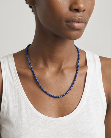 woman with a white tank top wearing 4mm blue lapis lazuli beaded necklace against a plain background