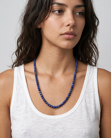 Woman wearing a 6mm blue lapis lazuli beaded necklace paired with a white tank top against a neutral background.