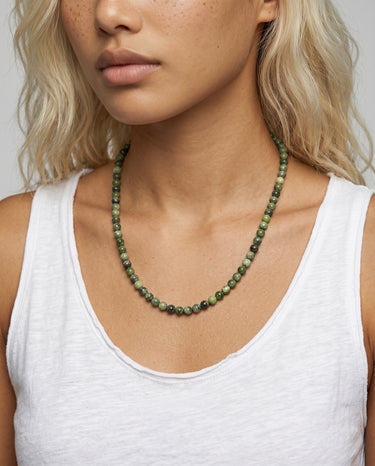 Woman wearing a chrome diopside beaded necklace against a neutral background
