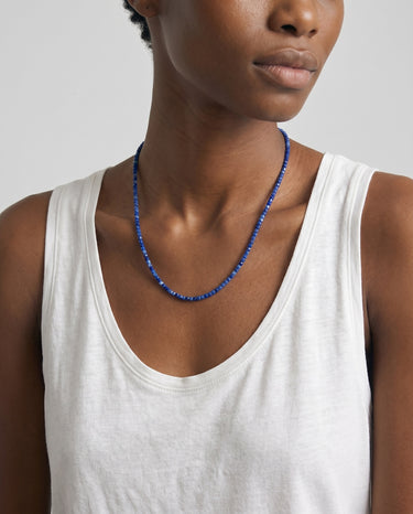 Woman with a white tank top is wearing a blue lapis lazuli beaded necklace with a plain background