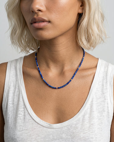 Woman wearing a blue faceted lapis lazuli cube beaded necklace against a neutral background