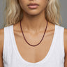 A studio shot of a woman wearing the 3mm faceted garnet cube necklace, showcasing its delicate scale and clean architectural drape against a white top.