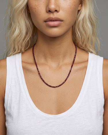 A studio shot of a woman wearing the 3mm faceted garnet cube necklace, showcasing its delicate scale and clean architectural drape against a white top.