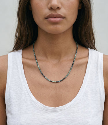 Woman wearing a white tank top and a faceted tourmaline beaded necklace against a neutral background