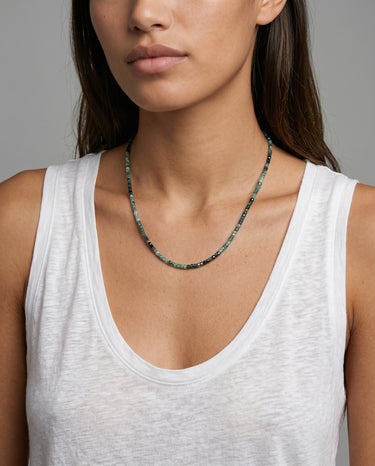 Woman wearing a white tank top and a faceted cube tourmaline beaded necklace against a neutral background