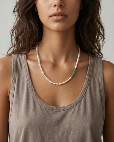 Woman wearing a white freshwater pearl necklace featuring 4–5mm pearls with an off-center stack of green Aventurine heishi disc beads and small metal accents.
