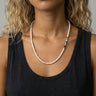 Woman wearing a white freshwater pearl necklace featuring 4–5mm pearls with an off-center stack of colorful millefiori round glass beads and small metal accents.
