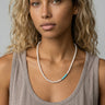 Woman wearing a handcrafted necklace featuring small white freshwater pearls and a short section of turquoise heishi disc beads, accented by a polished metal bead.