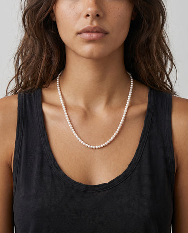 Woman wearing a pearl necklace against a neutral background