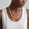 Woman wearing a pearl necklace and white tank top against a neutral background