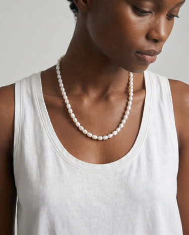 Woman wearing a pearl necklace and white tank top against a neutral background