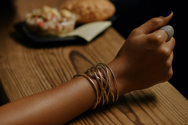 A close-up lifestyle shot of handcrafted 14K gold-filled and rose gold-filled cuff bracelets stacked on a model's wrist, emphasizing the unique, slight variances of the Chicago-made artisanal craftsmanship.
